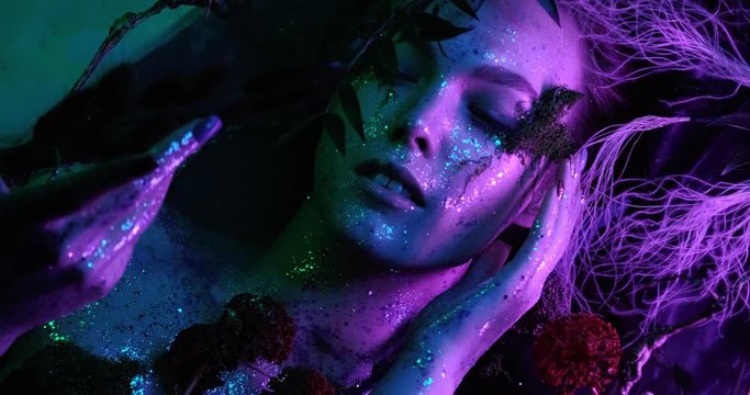 Fantasy world. Sexy beautiful girl model nymph lies in a mystical fog looking at the camera close-up in neon light with bright saturated colors. 4K video quality