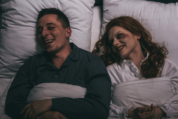 top view of smiling female demon lying in bed with man