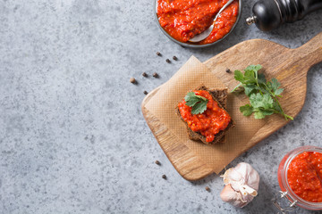 Slice of rye bread with ajvar. Vegetable sauce of baked red bell pepper on grey. Balkan cuisine. Space for text. Top view.