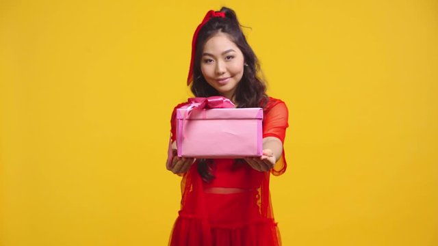 cheerful asian girl giving present isolated on yellow
