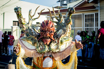 person in bright demon costume poses for photo on city street at dominican carnival - obrazy, fototapety, plakaty