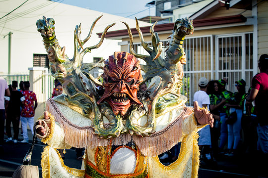 person in bright demon costume poses for photo on city street at dominican carnival