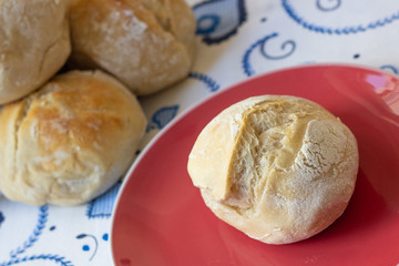 Destaque de pão branco tipo bola, típico de Portugal, sobre prato vermelho em mesa da cozinha com...