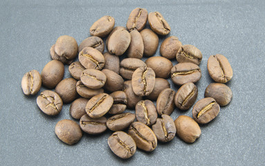 A scattered pile of roasted light brown coffee beans is scattered on a black textured background. Natural whole grains without processing