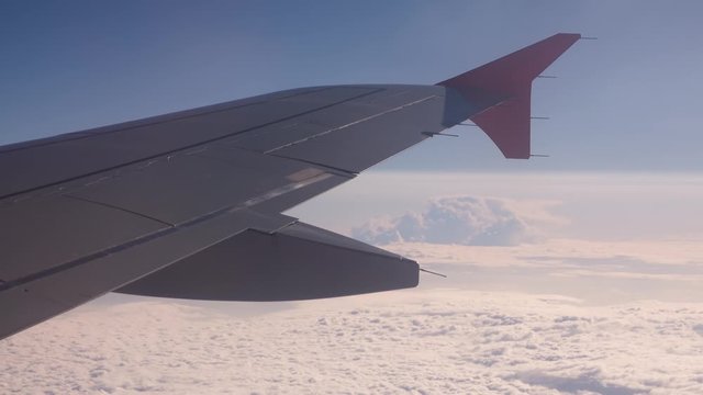 Wing of an airplane flying above the clouds. Footage of aerial view above clouds from airplane window with blue sky.