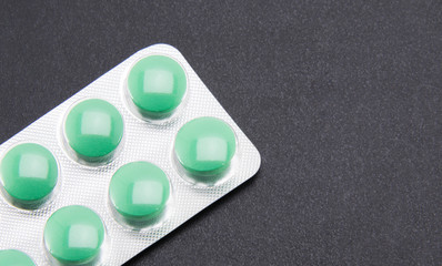 Unopened blister with green round pills on a black textured background. Part of the packaging in...
