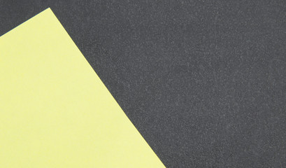 Abstract background of two colors. On a black, textured, rough background lies an obliquely light yellow sheet of paper (sticker). Close-up shot. Unusual creative template.  Part of a yellow blank.