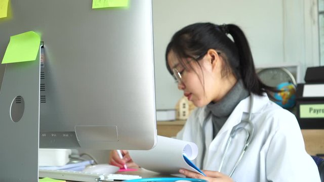 Asian doctor intern, medical student working or healthcare patients records on laptop computer with prescription, sitting in desk consultation with gown suite wearing stethoscope in clinic hospital,4K