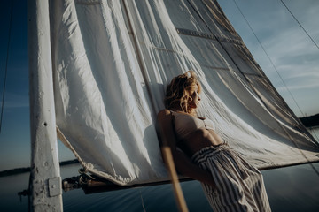 Woman stands on a yacht with white sails and looks at the sunset