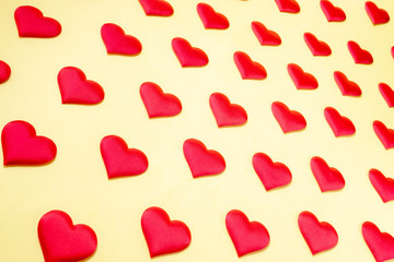 A lot of identical red silk hearts lying staggered on a yellow background. Symbol of love, tenderness and passion