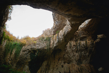 High arches of a huge stone cave with round holes at the top, a tourist road with a fence inside the cave. Bulgaria's natural attraction-Devetashka cave
