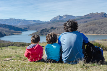 father and his two sons relaxing for a moment and enjoying the views after a hard hiking in the mountains of Palencia, Spain