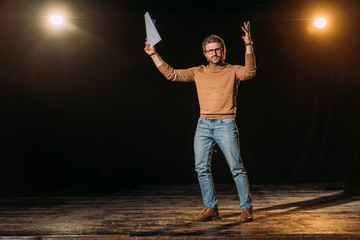 emotional theater director holding scenario and standing on stage during rehearse