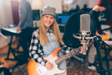 close up of studio microphone, blurred girl playing guitar in background