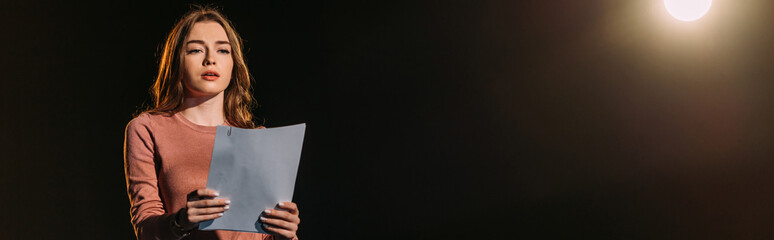 panoramic shot of attractive young actress reading scenario on black