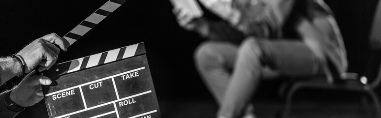 panoramic shot of actor with clapperboard in front, isolated on black, black and white