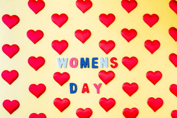 Multi-colored inscription, "Women's Day" in the middle of rhythmically arranged silk red hearts on a yellow background.  Postcard template for International Women's Day