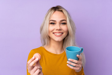 Teenager girl over isolated purple background holding colorful French macarons and a cup of milk