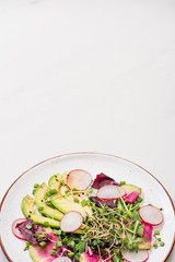 fresh radish salad with greens and avocado on plate on white surface