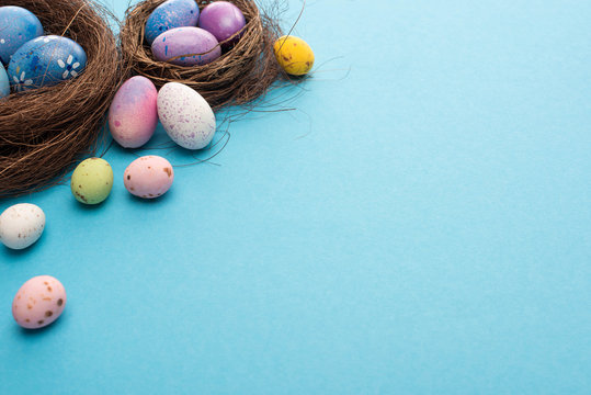 Nests with painted colorful chicken and quail eggs on blue background