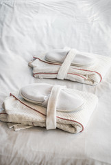 folded bathrobes and Slippers on the bed for hotel guests