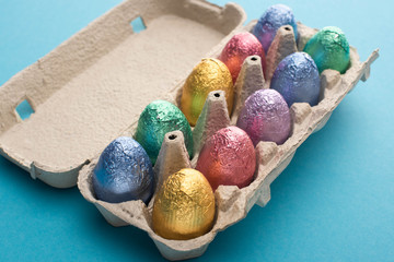Chocolate Easter eggs in colorful foil in egg tray on blue background