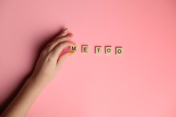 Woman hand making MeToo word with wooden alphabet on pink background, used for concept of sexual harrassment.