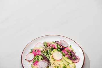fresh radish salad with greens and avocado on grey surface