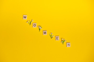 Top view word women spelled in wooden blocks on yellow background with flowers between them. Love,...