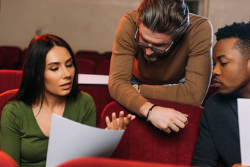 multiethnic young actor and actress reading screenplay with mature theater director