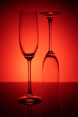 Two empty glasses of champagne with reflection, on a red and black background gradient background. Concept, party and club life.