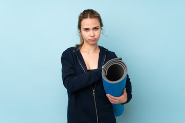 Teenager Russian girl holding mat isolated on blue background feeling upset © luismolinero