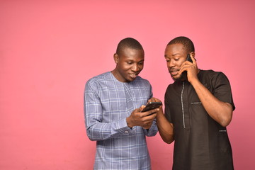 two young handsome african men wearing african attire viewing content on a mobile phone together