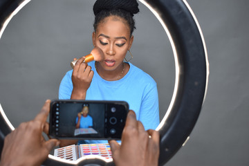 pretty young african woman filming a makeup tutorial to post online