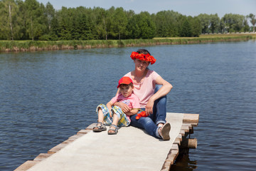 a young mother and her little son are sitting on the shore of the lake