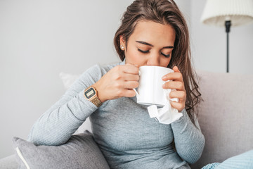 Sick woman with headache sitting under the blanket. Sick woman with seasonal infections, flu, allergy lying in bed. Sick woman covered with a blanket lying in bed with high fever and a flu, resting.