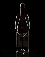 Bottle of red wine and a glass on black background. Subtle with highlights on edges. 