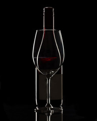 Bottle of red wine and a glass on black background. Subtle with highlights on edges. 