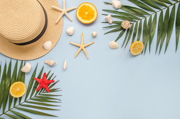 Flat lay summer vacation border frame. Palm leaves, fruits and seashells, straw hat on a blue background. Copy space in the middle