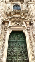 the main facade with bronze green bas-reliefs on the door of the Duomo of Milan