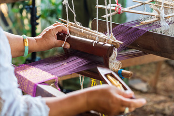 Traditional Isan Thai silk weaving. old woman hand weaving silk in traditional way at manual loom. Thailand. Selective focus.