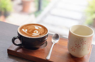 Hot latte art coffee in ceramic cup with tea cup on wooden table background