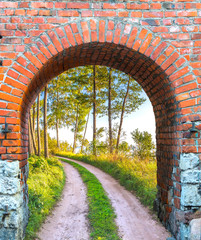 Old brick arch with entrance to the countryside road among pine forest