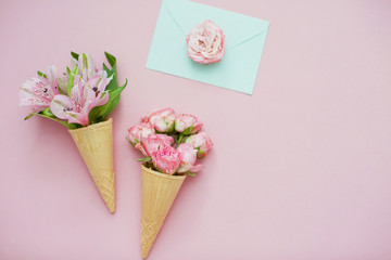 Ice cream cones with pink flowers and mint envelope on pink pastel background