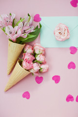 Ice cream cones with pink flowers and mint envelope on pink pastel background with heart shaped confetti
