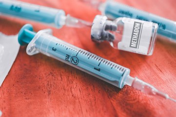 Spritze mit Kanüle auf einem Holztisch mit Medikament und Inschrift in deutsch Methadon in english methadone