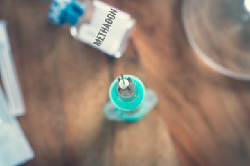 Spritze mit Kanüle auf einem Holztisch mit Medikament und Inschrift in deutsch Methadon in english...