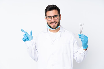 Dentist man holding tools isolated on white background pointing finger to the side