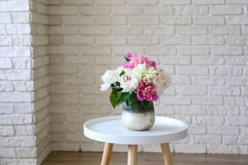 Empty apartment with minimal loft style interior, wooden floor and glass vase with bouquet of peonies on foreground and blank wall with a lot of copy space for text on background. Close up.