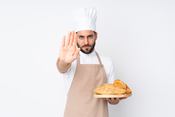 Male baker holding a table with several breads isolated on white background making stop gesture with her hand